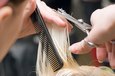 Blondes angefecuhtetes Haar wird mit einer Friseurschere geschnitten